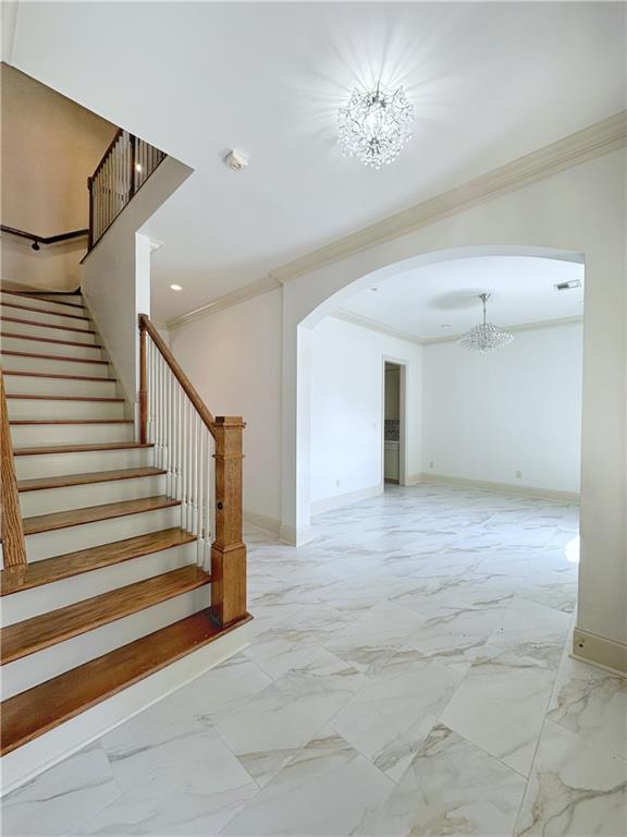 stairway with crown molding and an inviting chandelier