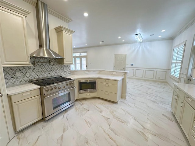 kitchen featuring crown molding, wall chimney exhaust hood, cream cabinetry, kitchen peninsula, and stainless steel appliances