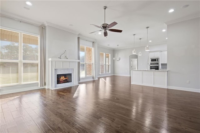 unfurnished living room featuring dark hardwood / wood-style flooring, crown molding, ceiling fan with notable chandelier, and a premium fireplace