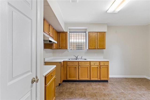 kitchen with under cabinet range hood, a sink, baseboards, light countertops, and brown cabinetry