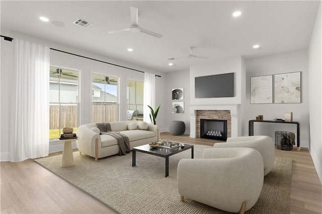 living room featuring light hardwood / wood-style flooring, a stone fireplace, ceiling fan, and a healthy amount of sunlight