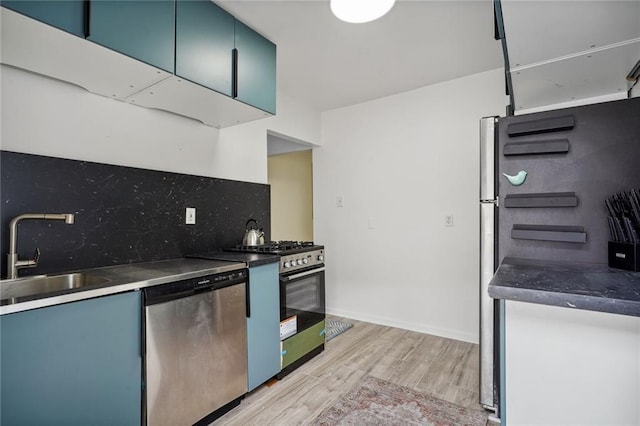 kitchen featuring tasteful backsplash, blue cabinets, sink, stainless steel appliances, and light wood-type flooring