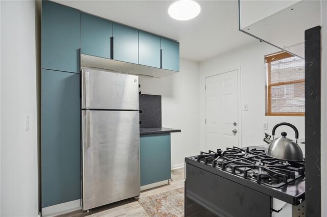 kitchen featuring gas range, stainless steel fridge, and blue cabinets