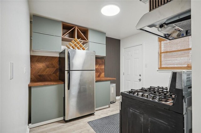 kitchen with ventilation hood, light wood-type flooring, stainless steel fridge, and black range with gas cooktop