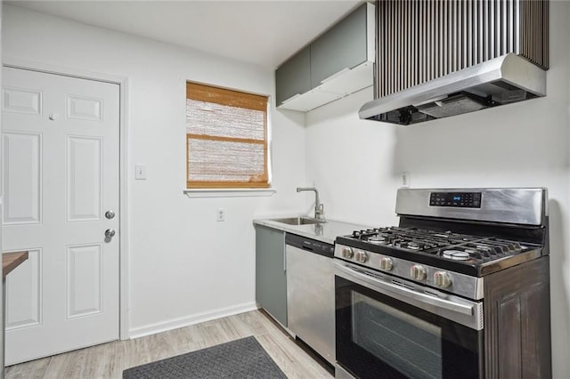 kitchen with stainless steel appliances, sink, wall chimney range hood, and light hardwood / wood-style flooring