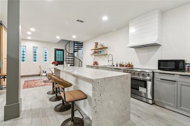 kitchen with gray cabinets, light wood-type flooring, light stone countertops, stainless steel stove, and a center island