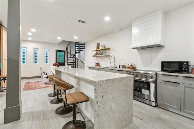 2604 Chartres St, New Orleans, LA 70130 - kitchen featuring high end stainless steel range oven, black microwave, custom range hood, a sink, and light wood-style flooring