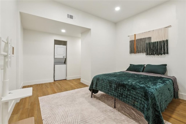 bedroom featuring wood-type flooring and stacked washer / drying machine