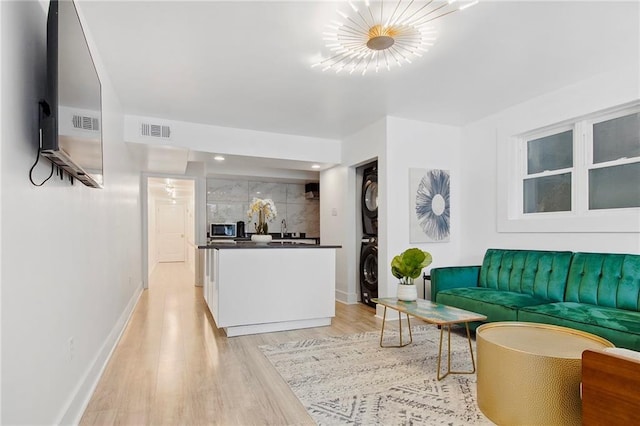 living room featuring light wood-type flooring, a chandelier, and stacked washer / dryer