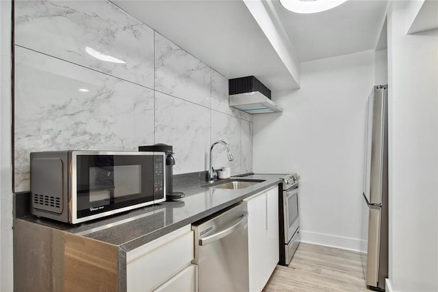 kitchen featuring wall chimney range hood, light hardwood / wood-style floors, sink, appliances with stainless steel finishes, and white cabinets