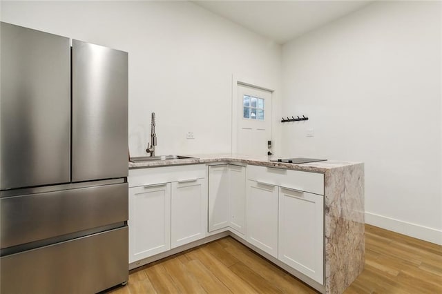 kitchen featuring sink, white cabinets, light wood-type flooring, and stainless steel refrigerator