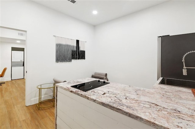 2604 Chartres St, New Orleans, LA 70130 - kitchen featuring stacked washer / dryer, black electric stovetop, light wood-style floors, light stone countertops, and a sink
