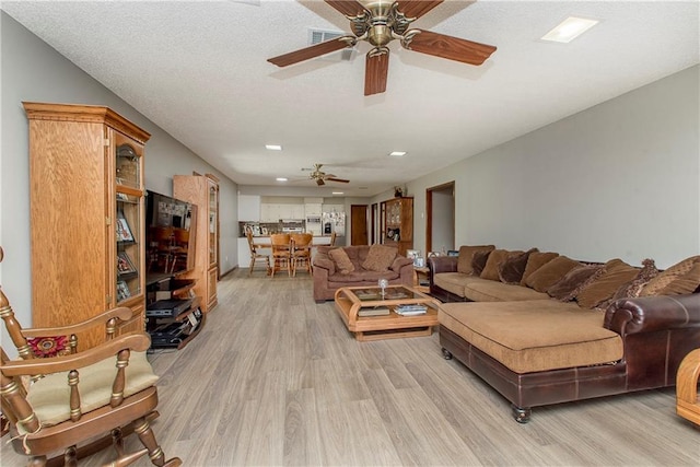 living room with ceiling fan, light hardwood / wood-style floors, and a textured ceiling