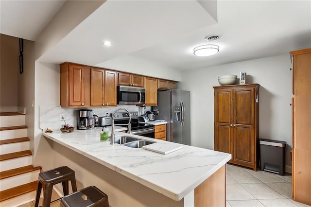 kitchen with kitchen peninsula, appliances with stainless steel finishes, a kitchen bar, light stone counters, and light tile patterned floors