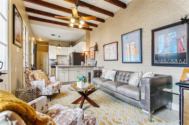 living room with ceiling fan, beam ceiling, and brick wall