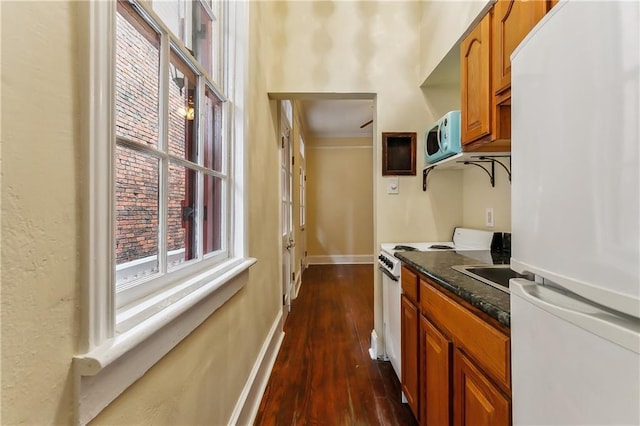 kitchen featuring dark stone countertops, white appliances, and dark wood-type flooring