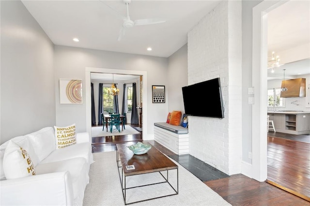 living room featuring a wealth of natural light, dark wood-type flooring, and ceiling fan with notable chandelier