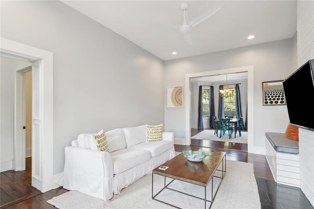 living room with ceiling fan with notable chandelier and dark hardwood / wood-style floors