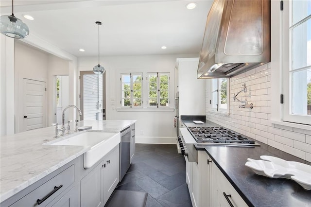 kitchen with hanging light fixtures, white cabinetry, sink, and range hood