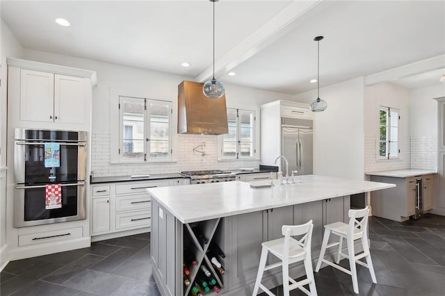 kitchen featuring white cabinetry, appliances with stainless steel finishes, decorative light fixtures, and a center island with sink