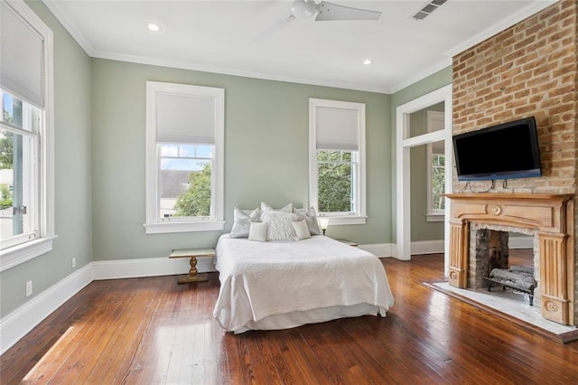 bedroom with crown molding, wood-type flooring, ceiling fan, and a fireplace