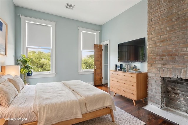 bedroom with a brick fireplace and dark wood-type flooring