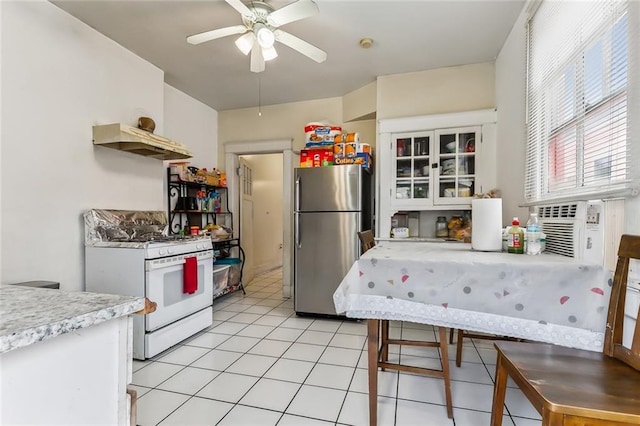 kitchen with white cabinetry, white gas stove, ceiling fan, stainless steel fridge, and exhaust hood