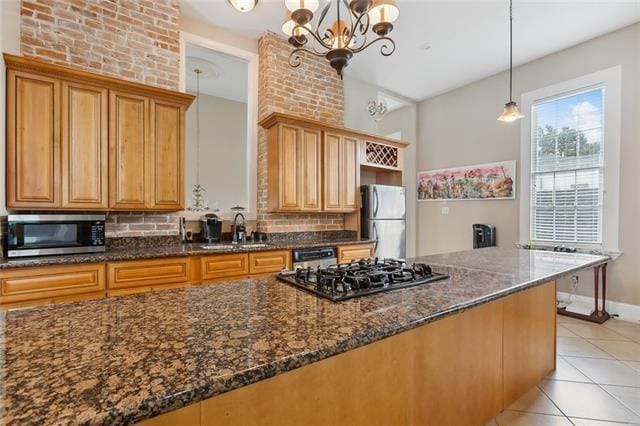 kitchen featuring appliances with stainless steel finishes, dark stone counters, sink, pendant lighting, and a notable chandelier