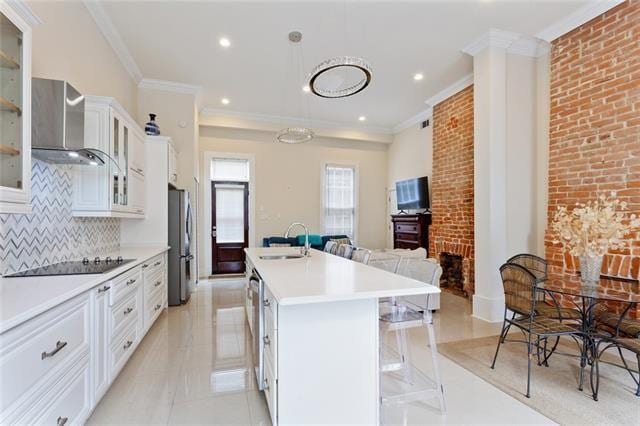 kitchen featuring a center island with sink, white cabinetry, a kitchen bar, and wall chimney range hood