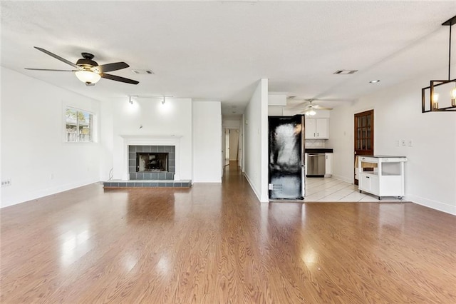 unfurnished living room with light wood-type flooring, a tiled fireplace, and ceiling fan with notable chandelier