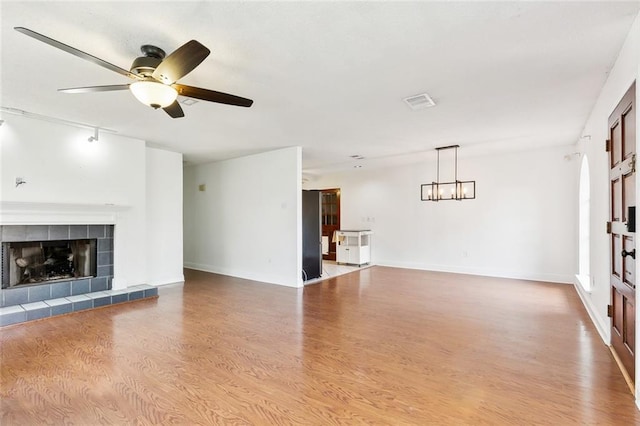 unfurnished living room with hardwood / wood-style flooring, a tiled fireplace, and ceiling fan with notable chandelier