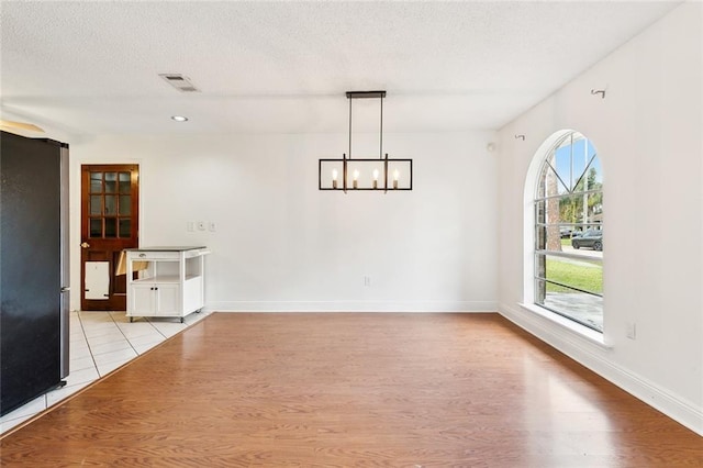 empty room featuring plenty of natural light, a notable chandelier, and light hardwood / wood-style flooring