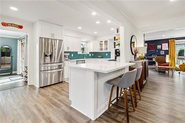 kitchen with a kitchen breakfast bar, light wood-type flooring, backsplash, stainless steel appliances, and white cabinetry