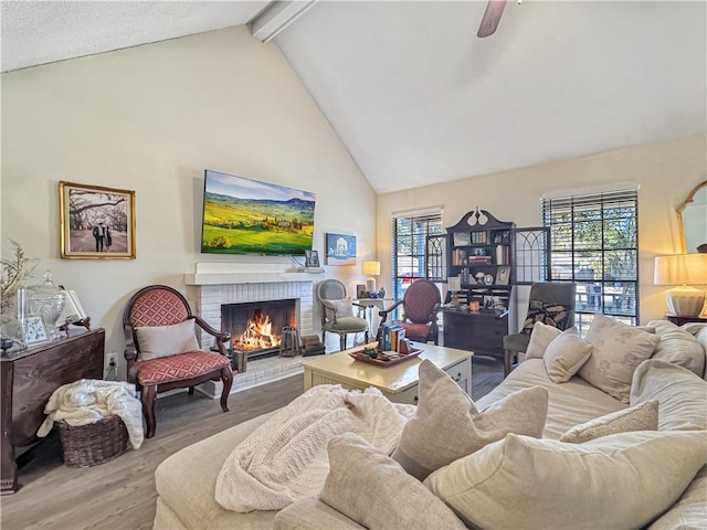 living room featuring beam ceiling, ceiling fan, a brick fireplace, high vaulted ceiling, and wood-type flooring