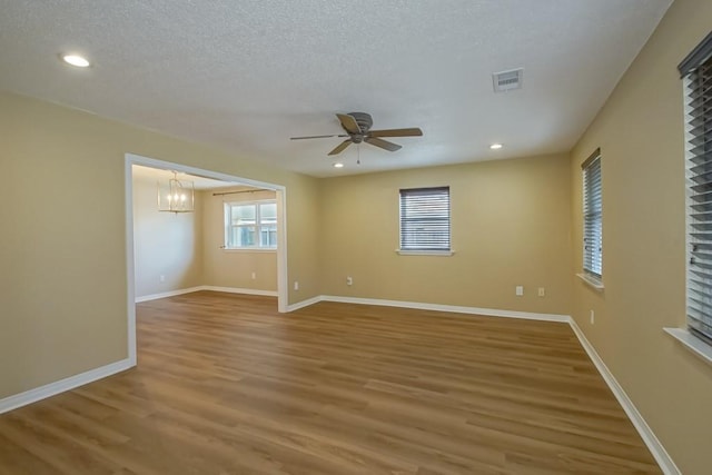 unfurnished room featuring a textured ceiling, wood-type flooring, and ceiling fan with notable chandelier