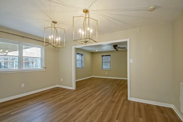 spare room with wood-type flooring, ceiling fan with notable chandelier, and a textured ceiling