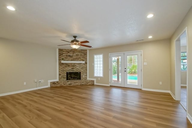 unfurnished living room with a fireplace, ceiling fan, french doors, and light hardwood / wood-style flooring