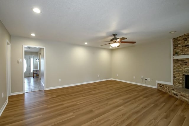 unfurnished living room featuring ceiling fan, hardwood / wood-style floors, a textured ceiling, and a brick fireplace