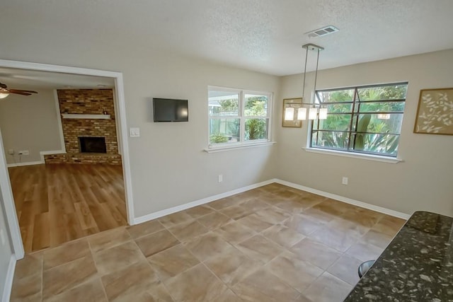 unfurnished dining area featuring a textured ceiling, ceiling fan, and a fireplace