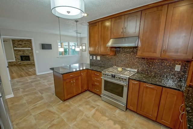 kitchen featuring dark stone counters, decorative light fixtures, decorative backsplash, a fireplace, and stainless steel stove