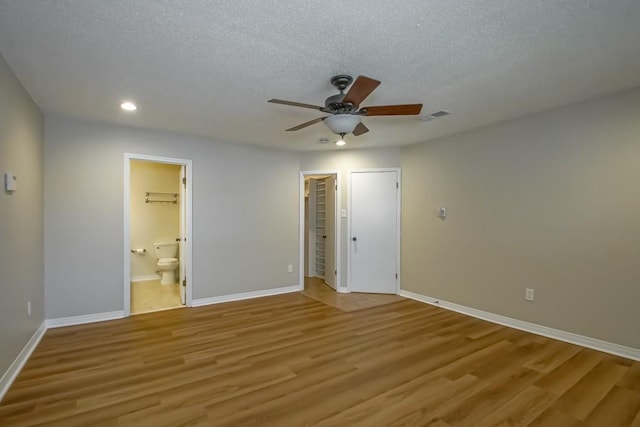 unfurnished bedroom with ensuite bath, a textured ceiling, ceiling fan, light hardwood / wood-style flooring, and a closet