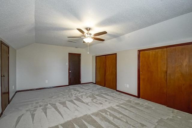 unfurnished bedroom with light carpet, a textured ceiling, vaulted ceiling, ceiling fan, and multiple closets