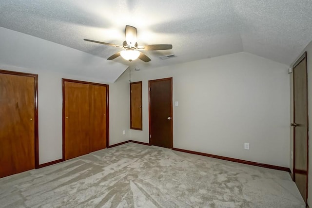 unfurnished bedroom featuring ceiling fan, lofted ceiling, light carpet, and two closets