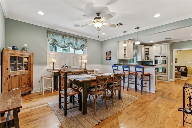 dining area with a ceiling fan, light wood-type flooring, visible vents, and crown molding