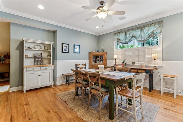 dining space featuring ornamental molding, wainscoting, light wood finished floors, and a ceiling fan