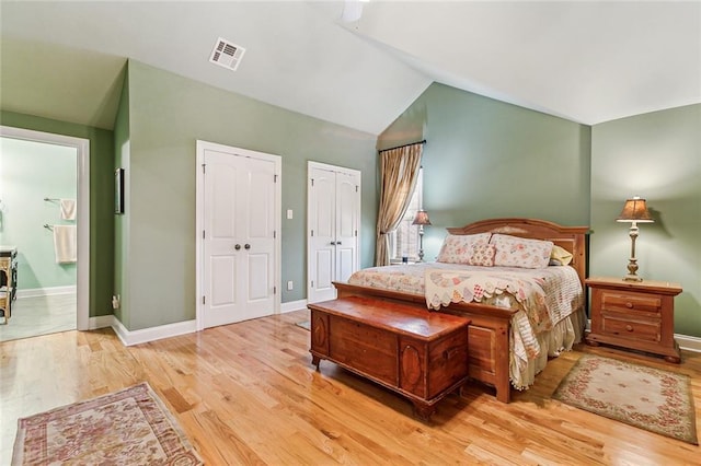 bedroom featuring baseboards, visible vents, wood finished floors, vaulted ceiling, and two closets