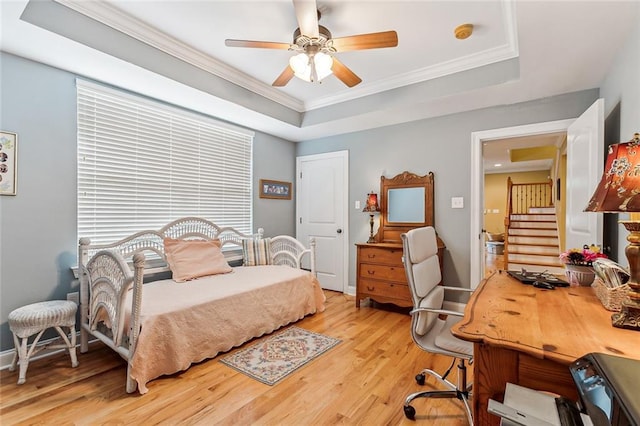 bedroom featuring a ceiling fan, baseboards, light wood-style floors, a raised ceiling, and crown molding