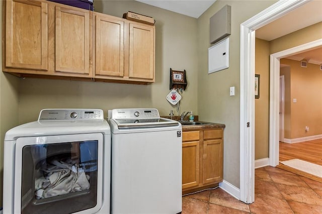 washroom featuring cabinet space, baseboards, a sink, and washing machine and clothes dryer