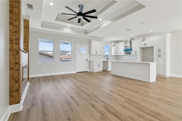 unfurnished living room featuring ceiling fan, sink, a raised ceiling, crown molding, and light wood-type flooring