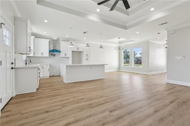 unfurnished living room featuring ceiling fan with notable chandelier, ornamental molding, light hardwood / wood-style flooring, and a tray ceiling